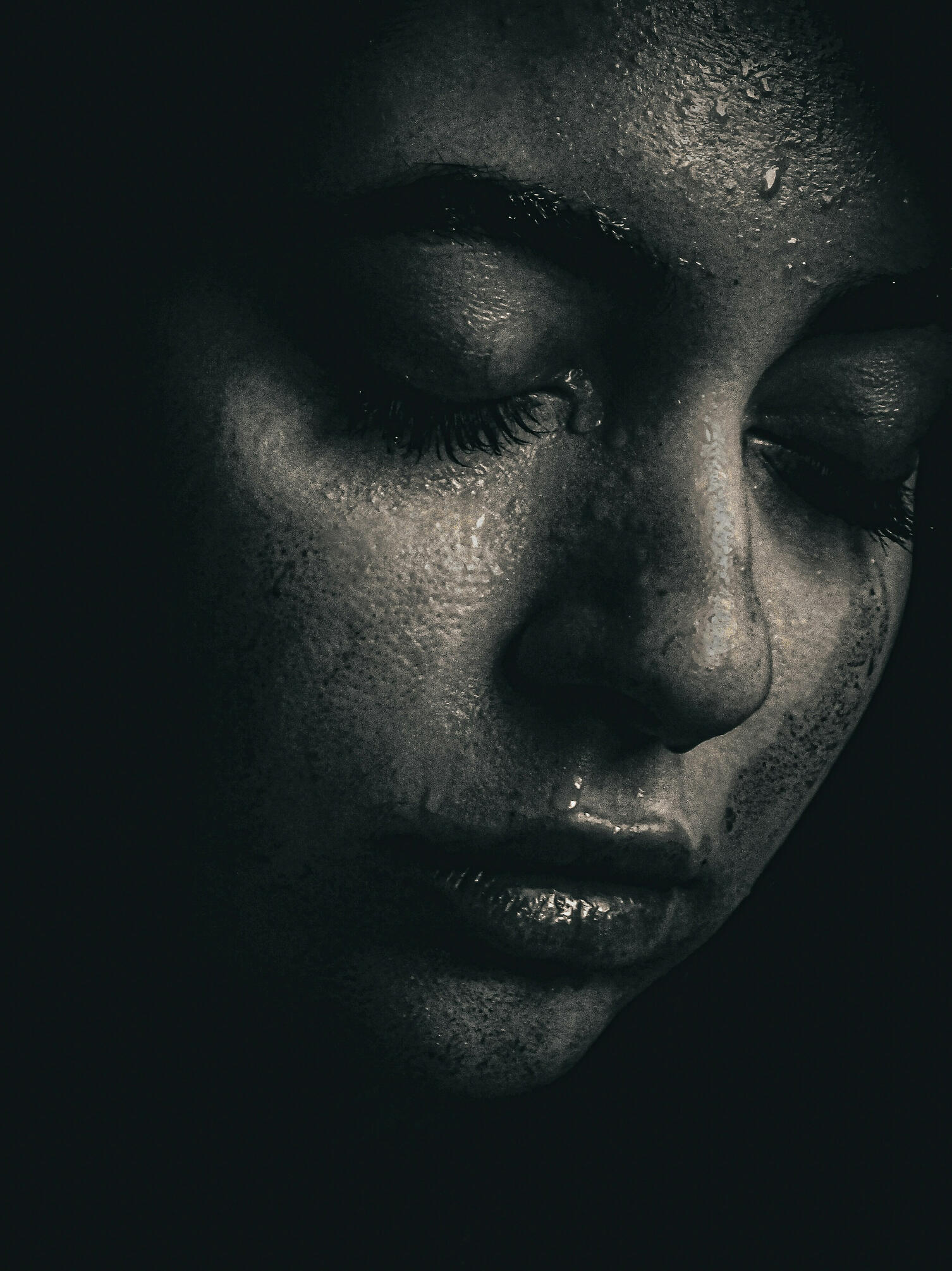 Photographie artistique en noir et blanc d'un visage de femme de profil partiel, yeux clos, avec des gouttelettes d'eau et une texture de peau très détaillée. Style clair-obscur intense.